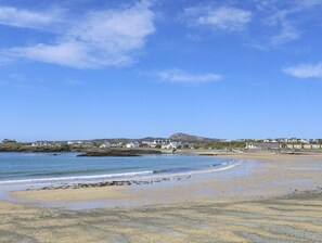 A coastal beach with a clear sky, sandy shore, and buildings in the background. - Towyn Lodge (Holyhead)