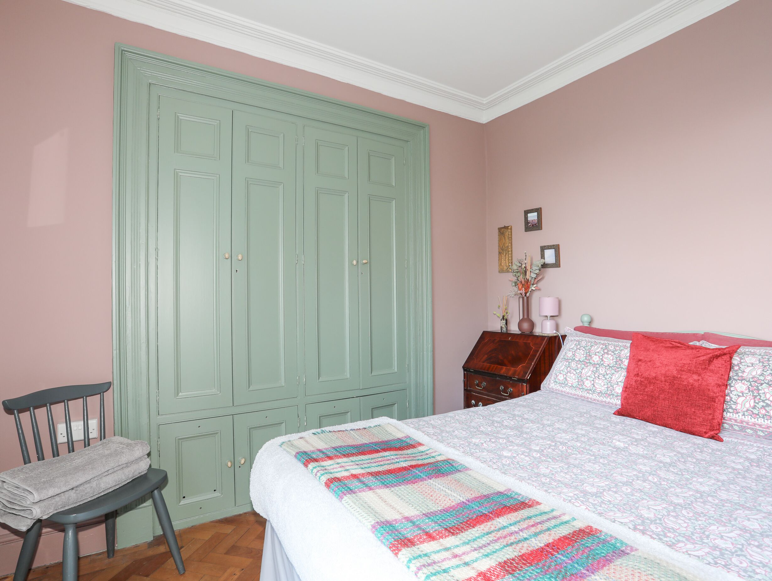 Un dormitorio con cama, una silla, armario y cómoda.