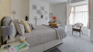A bedroom with a bed, bedside table, lamp, chair, and a window with curtains. - Sunny Days (Weymouth)