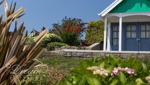 A cottage with a green roof, white walls, and a stone wall in front. - Sunny Days (Weymouth)