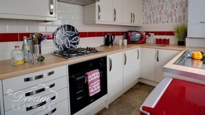 A kitchen with white cabinets, a gas stove, a microwave, and a red countertop. - Sunny Days (Weymouth)