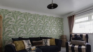 A living room with a sectional sofa, a round ottoman, and a striped armchair. - Sunny Days (Weymouth)