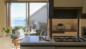Une cuisine moderne dotée d’une cuisinière intégrée, un coin repas avec une table et des chaises, et une vue sur la mer grâce à de grandes fenêtres.