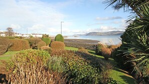 Un jardin aménagé avec des arbustes taillés avec soin, offrant une vue sur un plan d’eau et sur des collines lointaines.