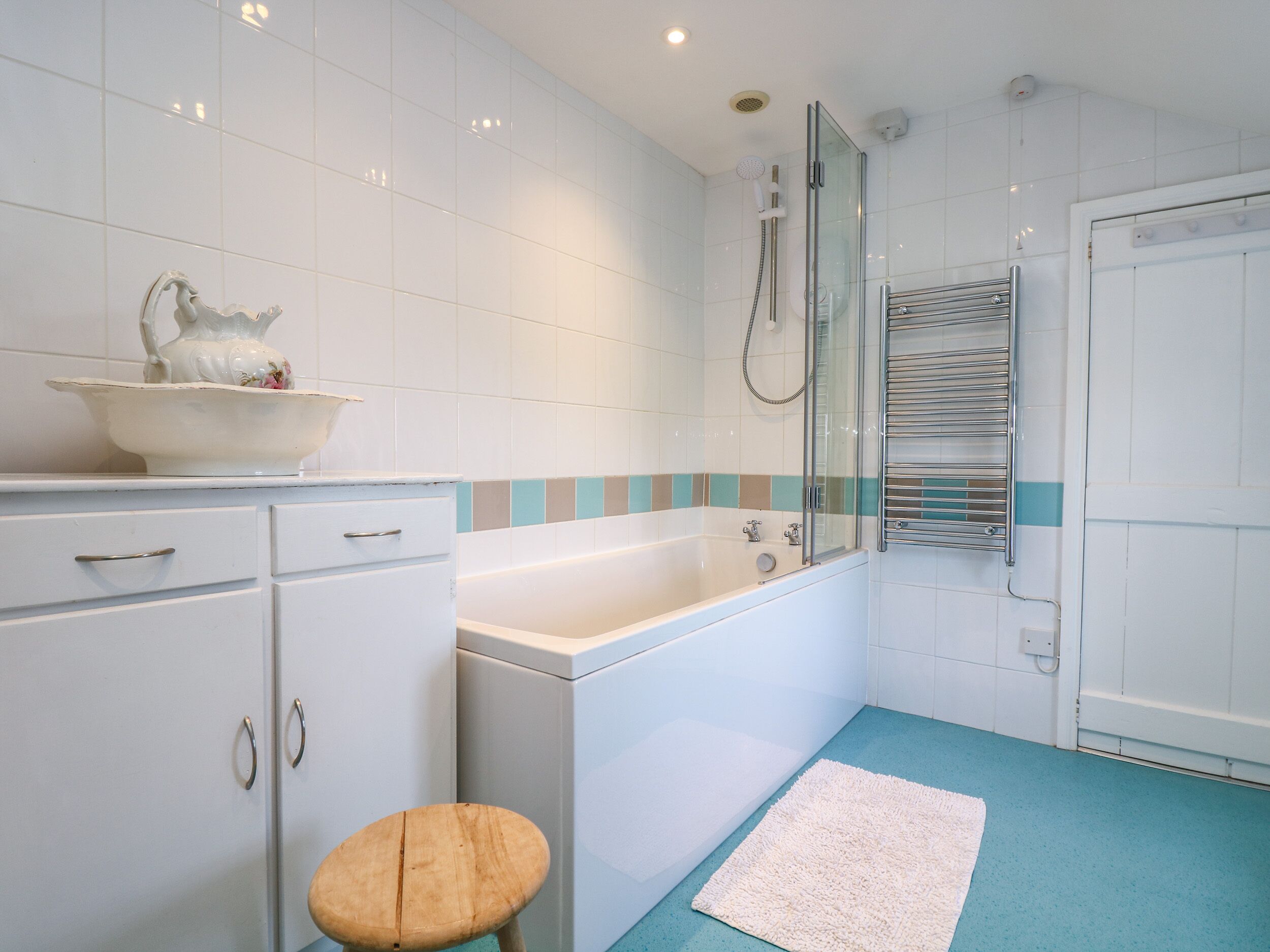 Ein Badezimmer mit einer Badewanne, einer Duschkabine aus Glas, einem Waschbecken mit dekorativer Schale und einem hölzernen Hocker.