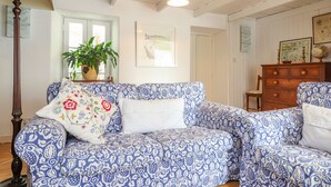 Uma sala de estar aconchegante com um sofá estampado, piso de madeira, uma janela grande com vista e um ventilador de teto.