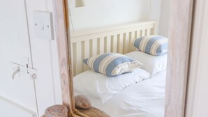 Quarto com cama branca, almofadas listradas e prateleira de madeira com corda.
