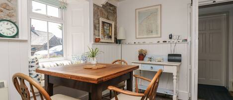 A cozy kitchen with a wooden table and chairs, a window with a view, and a stone wall.