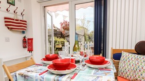 A dining area with a table set for four, red and white striped beach towels, a fire extinguisher, and a view of the garden through the window. - White Haven (Sandown)