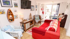 A living room with a red sofa, a white armchair, a wooden cabinet, and a television on the wall. - White Haven (Sandown)