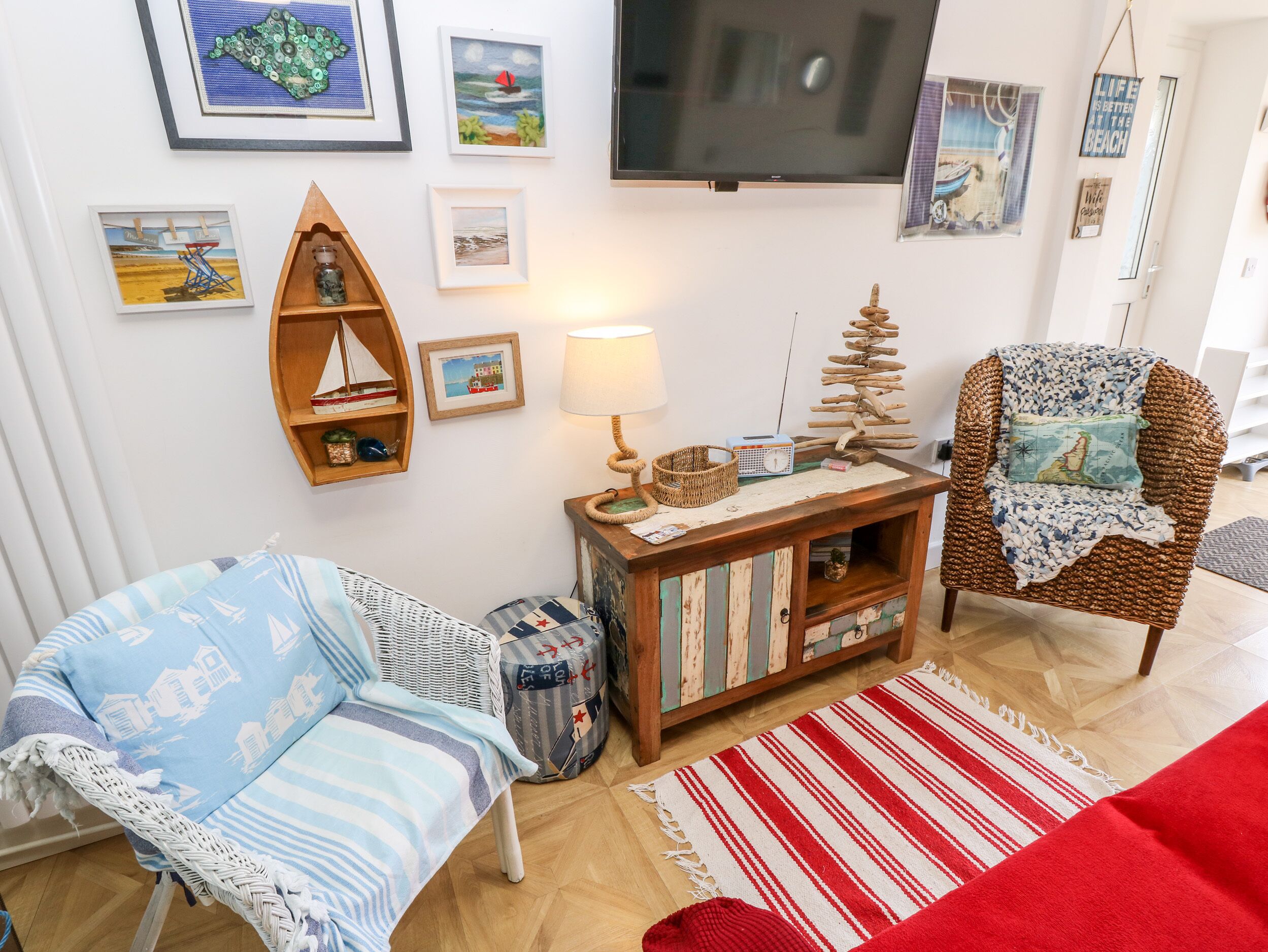 A cozy living room with a blue and white striped chair, a wooden side table with a lamp, a red and white striped rug, and various framed artworks on the wall.