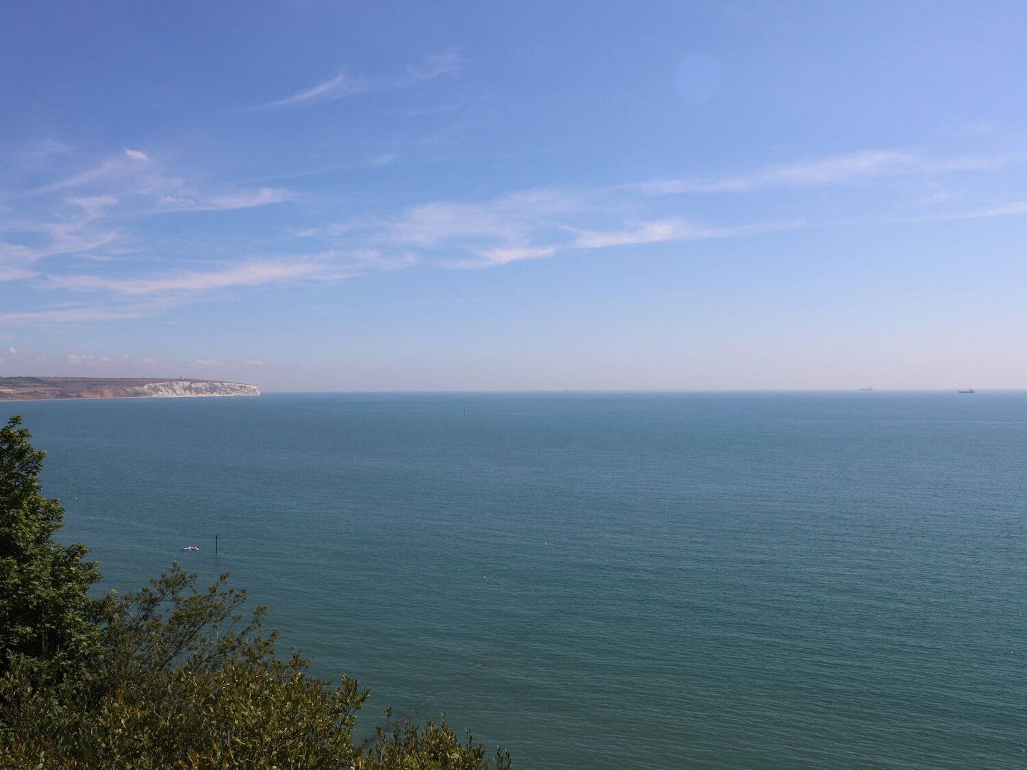 A coastal view with calm sea, distant land, and clear sky.