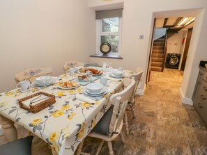 A dining area with a table set for four, chairs, a window with a clock, and a view of a laundry room.