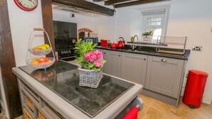 A kitchen with a marble countertop, a red kettle, and a basket of flowers. - Hafodty (Conwy)