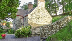 A stone building with a gravel path, a wooden bench, and a flower bed with pink flowers. - Hafodty (Conwy)