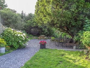 A garden with a gravel path, a wooden bench, and a table with chairs.