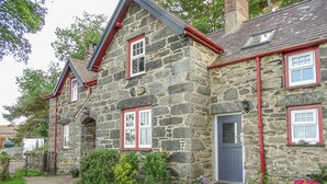 A stone house with red-framed windows and a door, surrounded by a gravel path and greenery. - Hafodty (Conwy)