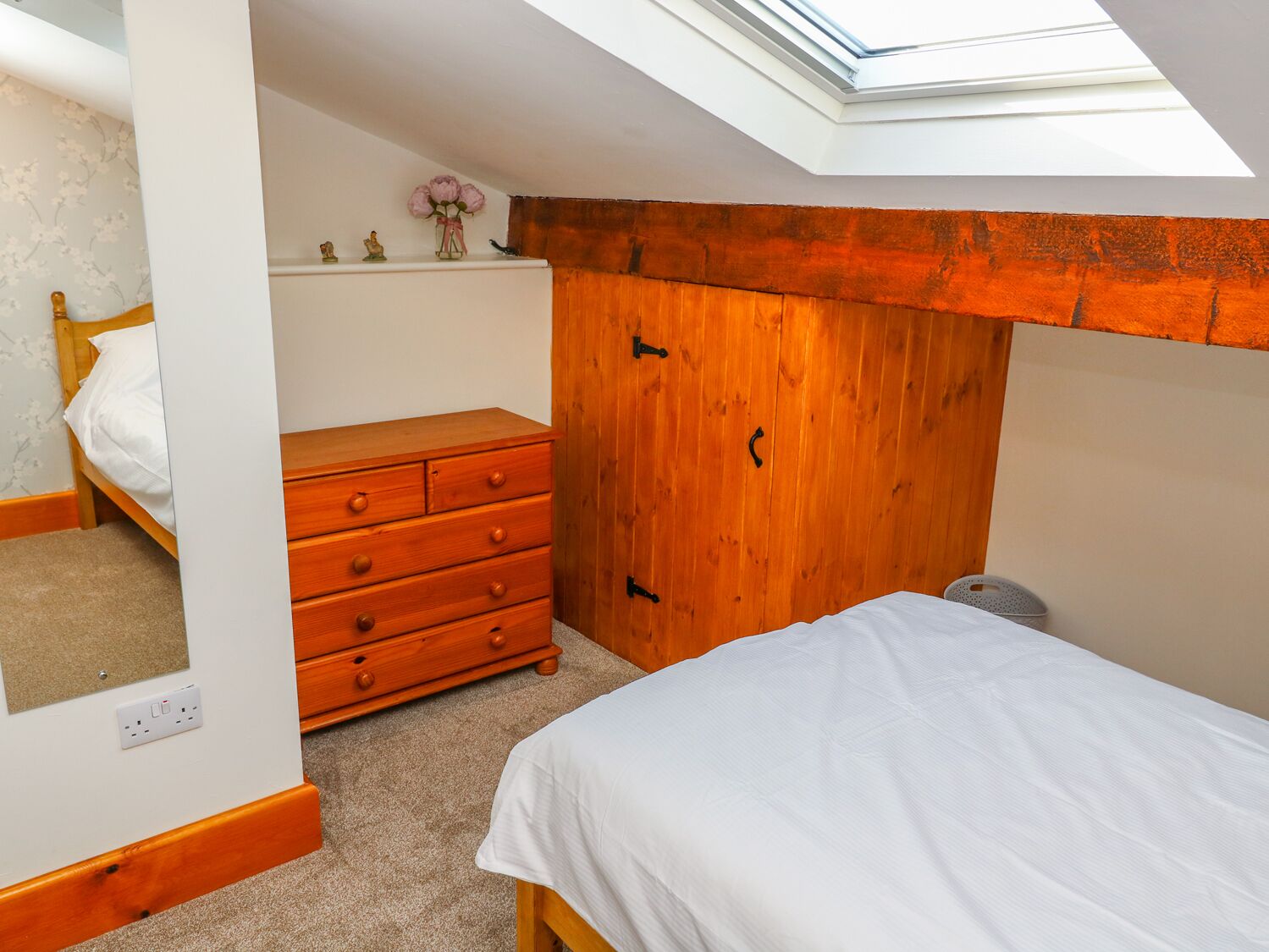 A bedroom with a skylight, a wooden wardrobe, a bed, and a small dresser.