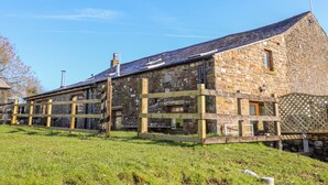A stone building with a sloped roof, wooden fence, and a grassy area in front. - Stable View Cottage (Clitheroe)