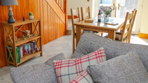 A cozy living room with a wooden staircase, a dining table with chairs, a bookshelf, and a grey sofa with plaid cushions. - Stable View Cottage (Clitheroe)