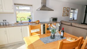 A modern kitchen with white cabinets, a wooden dining table, and a view of the outdoors. - Stable View Cottage (Clitheroe)