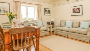 A cozy living room with a dining table set for four, a sofa, a small side table, and a window with curtains.
