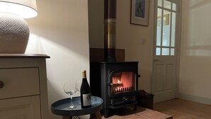 A cozy room with a wood-burning stove, a wine bottle, and glasses on a small table.
