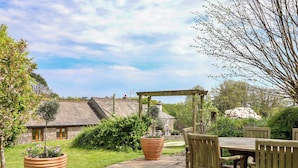 A patio with a table and chairs, surrounded by potted plants and a stone pathway. - Erin Cottage (Looe)