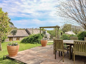 A patio with a table and chairs, surrounded by potted plants and a stone pathway. - Erin Cottage (Looe)
