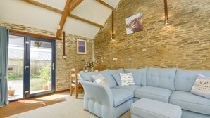 A cozy living room with a light blue sectional sofa, a stone wall, and a wooden ceiling. - Erin Cottage (Looe)