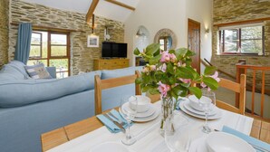 A dining area with a table set for four, a sofa, and a stone wall. - Erin Cottage (Looe)
