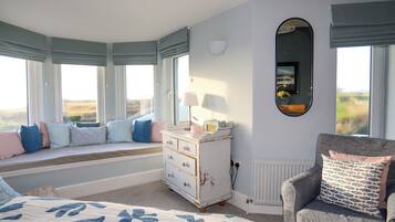 Un dormitorio con una cama grande, un aparador, una silla y un rincón con asiento junto a la ventana que da a un paisaje.