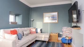 A modern living room with a light-colored sectional sofa, a patterned rug, a framed picture on the wall, and a television mounted on the wall.