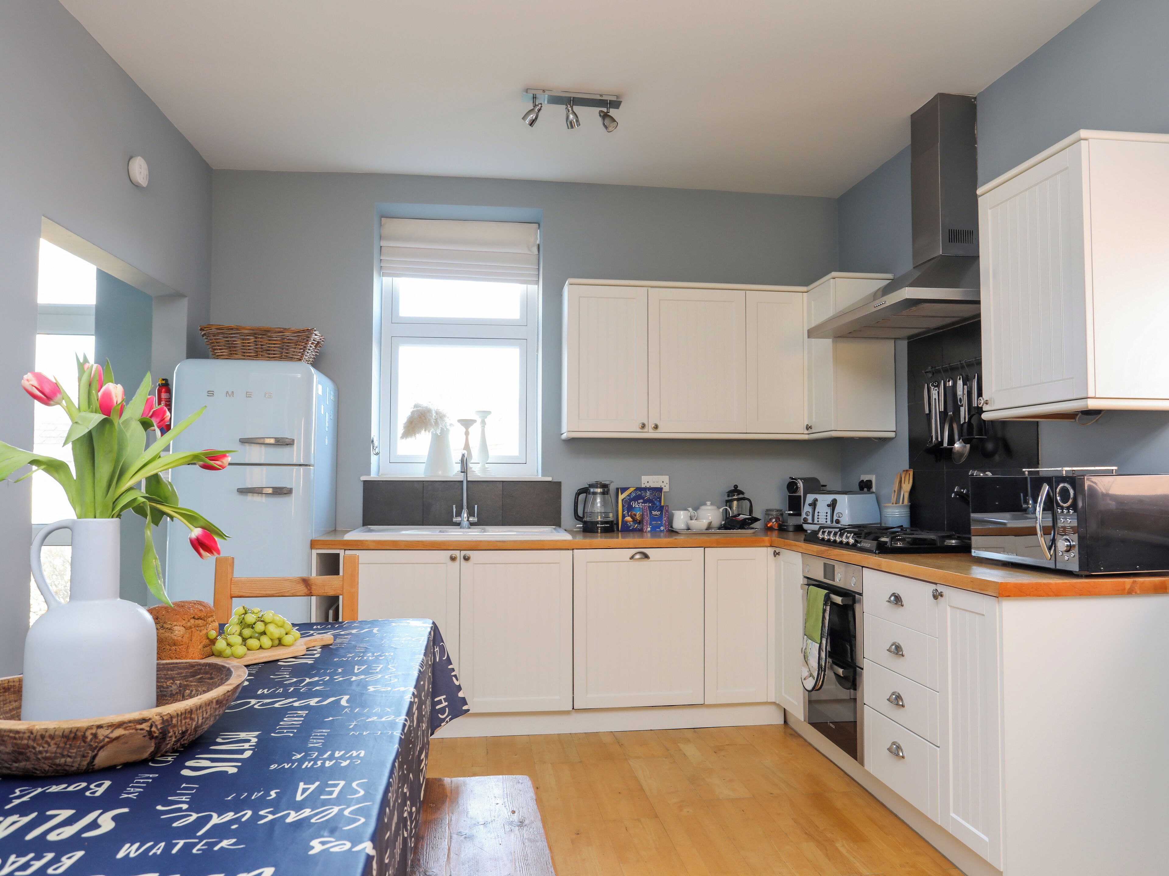 A modern kitchen with white cabinets, a wooden countertop, and a window with blinds.