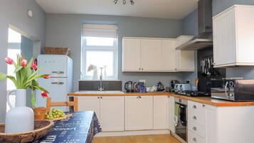 A modern kitchen with white cabinets, a wooden countertop, and a window with blinds.
