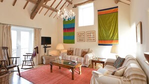 A spacious living room with a high ceiling, wooden beams, a chandelier, a large window, and a red carpet. - Cefn Isaf (Porthmadog)