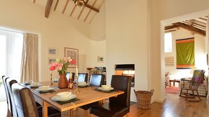 A dining area with a wooden table set for four, surrounded by chairs. There is a fireplace in the background, and a wicker basket is visible on the floor. - Cefn Isaf (Porthmadog)