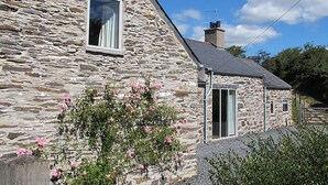 A stone house with a triangular roof, a chimney, and a small door. - Cefn Isaf (Porthmadog)