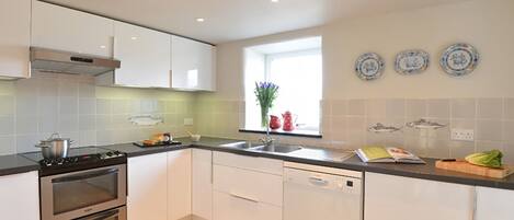 Une cuisine moderne avec des meubles blancs, une cuisinière, un four, un lave-vaisselle et une fenêtre ornée d’assiettes décoratives.