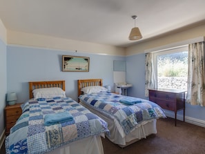 A bedroom with two beds, a bedside table with a lamp, a dresser, a window with curtains, and a painting on the wall. - Waterson (Weymouth)