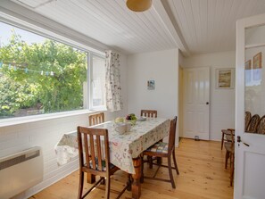 A dining area with a table set for four, wooden chairs, a window with curtains, and a white door. - Waterson (Weymouth)