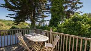 Une terrasse en bois avec une table ronde et quatre chaises, entourée d’une balustrade en bois.