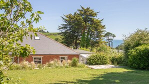 Une maison avec un toit en pente, une façade en briques et un jardin comprenant une pelouse et diverses plantes.