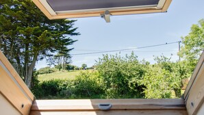 Une terrasse en bois dotée d’une lucarne, offrant une vue sur un paysage verdoyant, avec des arbres et un ciel dégagé.