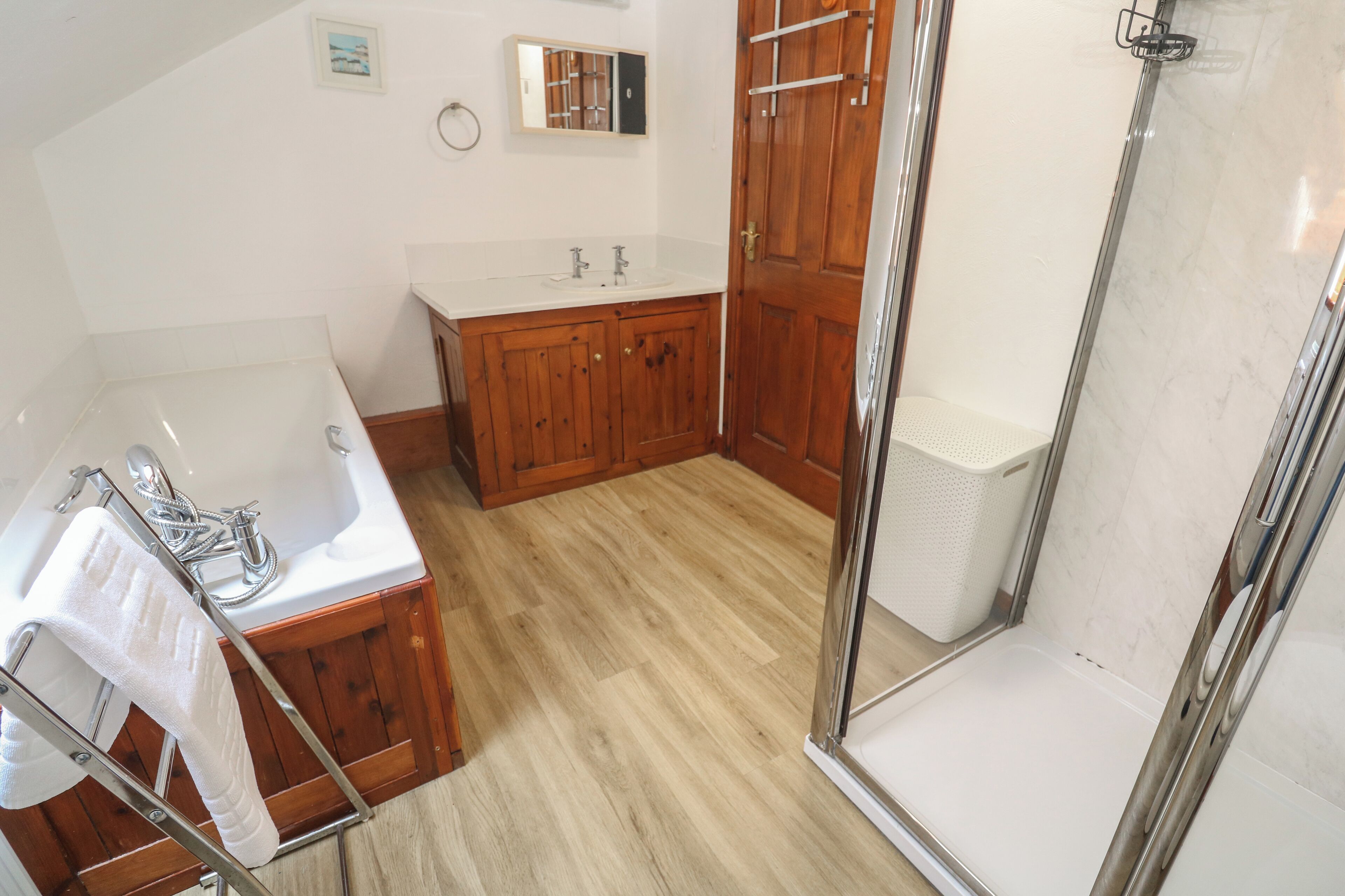 A bathroom with a wooden vanity, a bathtub, a shower area, and a white sink.