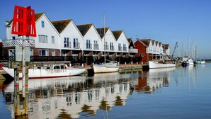 A row of white houses with red roofs by a calm water body, boats docked, and a red sign in the foreground.