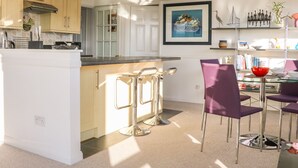 Een moderne keuken met een centraal eiland, barkrukken en een eethoek met paarse stoelen.