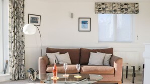 Een woonkamer met een bruine bank, een glazen salontafel en twee ingelijste foto's aan de muur.