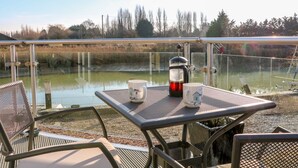 Een tafel met een koffiezetapparaat en twee mokken, met uitzicht op een waterpartij met een glazen balustrade.