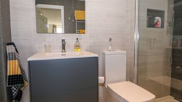 Un baño moderno con un espejo grande, un lavabo, un inodoro y una zona de ducha.
